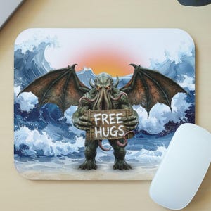 May include: A square mousepad featuring a green, winged, tentacled creature standing on a sandy beach before crashing ocean waves. The creature holds a wooden sign with the text "FREE HUGS" written in white letters against a sunset background.