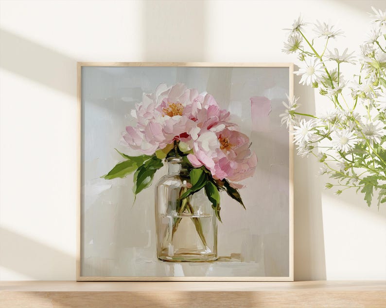 May include: A square framed print featuring a still life of pink peonies in a clear glass vase. The painting has a soft, impressionistic style with visible brushstrokes. Green leaves and white flowers are also visible.