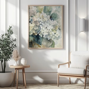 May include: A framed watercolor print featuring a cluster of white and blue hydrangea flowers with green leaves. The artwork has a soft, muted color palette and is displayed in a light wood frame, suitable for home decor.