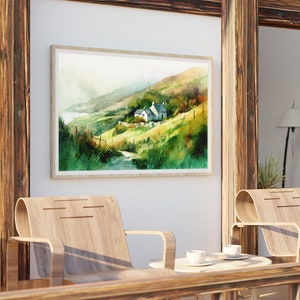 May include: A watercolor painting of a white cottage nestled in a green hillside with a winding path leading to it. The painting is framed and hanging on a white wall.