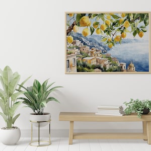 May include: A watercolor painting of a lemon tree with yellow lemons hanging from the branches. The tree is in front of a cityscape with buildings on a hillside overlooking the ocean. The painting is framed in a light wood frame and hanging on a white wall.
