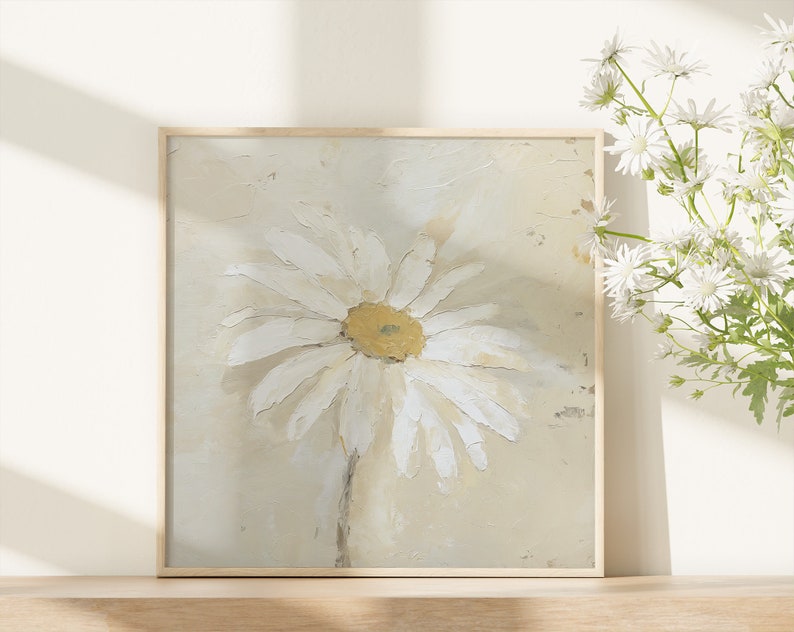 May include: A framed painting of a white daisy with a yellow center on a beige background.