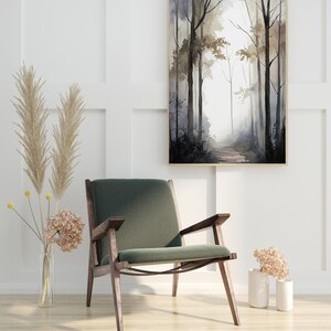 May include: A green velvet armchair with dark wood legs sits in front of a white wall with a framed watercolor painting of a forest path. The painting features a light gray background with dark gray trees and a light brown path.