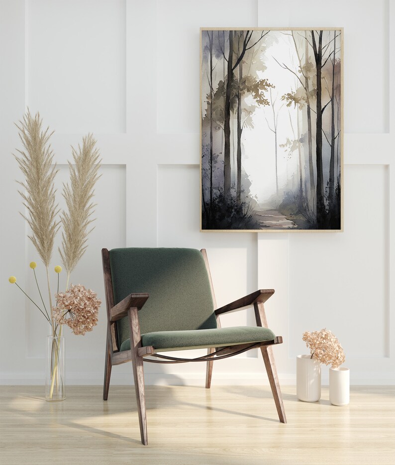 May include: A green velvet armchair with dark wood legs sits in front of a white wall with a framed watercolor painting of a forest path. The painting features a light gray background with dark gray trees and a light brown path.