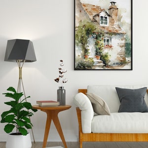 May include: A watercolor painting of a small cottage with a brown roof, white walls, and green vines growing on the side. The cottage has a window with a view of a green field and a small porch with a door. The painting is framed in black and hangs on a white wall.