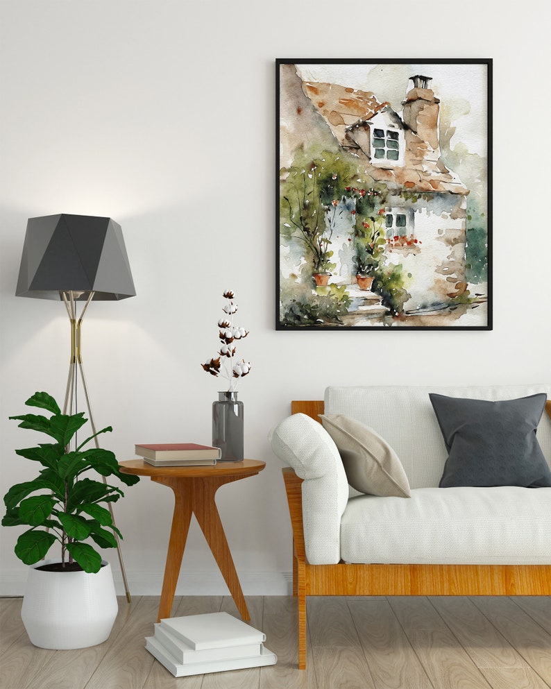 May include: A watercolor painting of a small cottage with a brown roof, white walls, and green vines growing on the side. The cottage has a window with a view of a green field and a small porch with a door. The painting is framed in black and hangs on a white wall.