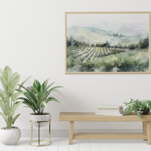 May include: A framed watercolor painting of a vineyard landscape with rolling hills and a hazy sky. The painting is hanging on a white wall above a wooden bench with a stack of books and two potted plants.