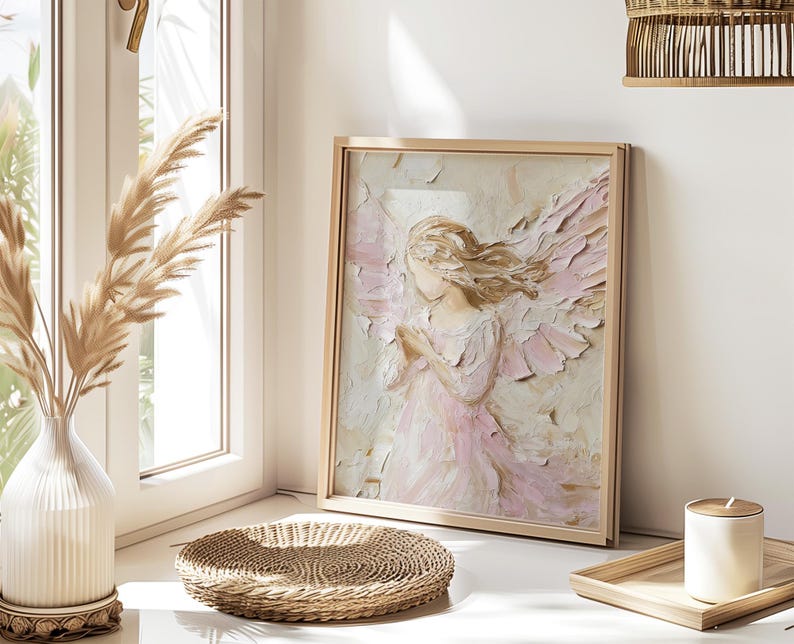 May include: A framed painting of a delicate angel with soft pink and white wings. The angel is depicted with a gentle expression and is wearing a flowing white dress. The painting is set against a light background and is framed in a simple wooden frame.