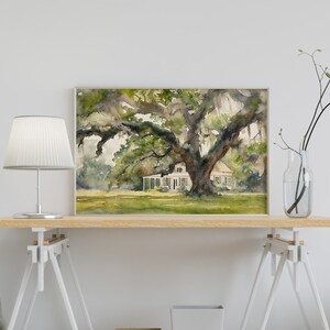 May include: A watercolor painting of a white house with a large oak tree in front of it. The house has a porch and a white roof. The tree has green leaves and long branches that hang down. The painting is framed in a light wood frame.