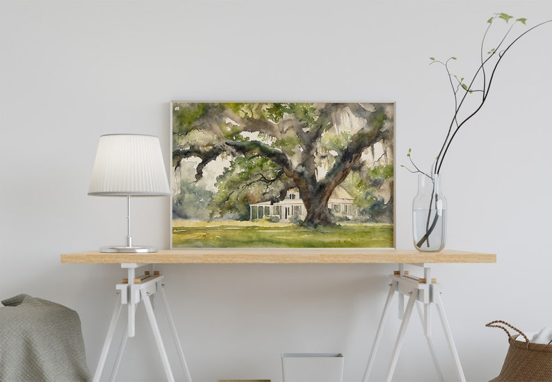 May include: A watercolor painting of a white house with a large oak tree in front of it. The house has a porch and a white roof. The tree has green leaves and long branches that hang down. The painting is framed in a light wood frame.