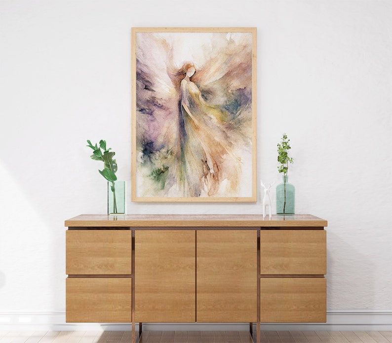 K&ouml;nnte beinhalten: Ein Aquarellbild einer Frau mit Fl&uuml;geln in Violett-, Gr&uuml;n- und Braunt&ouml;nen, gerahmt in einem hellen Holzrahmen, das &uuml;ber einem Holzschrank h&auml;ngt.