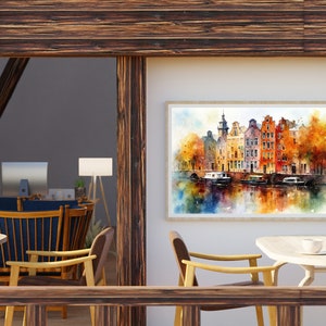 May include: A watercolor painting of a canal scene with colorful buildings and boats. The painting is framed and hanging on a white wall in a room with wooden beams and a table with chairs.