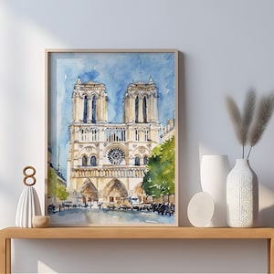 Op de afbeelding: Een aquarel schilderij van de Notre Dame kathedraal in Parijs, Frankrijk. Het schilderij is ingelijst en hangt aan een muur boven een houten consoletafel. De consoletafel heeft een witte vaas met gedroogd pampasgras en een wit keramiek beeldje erop.