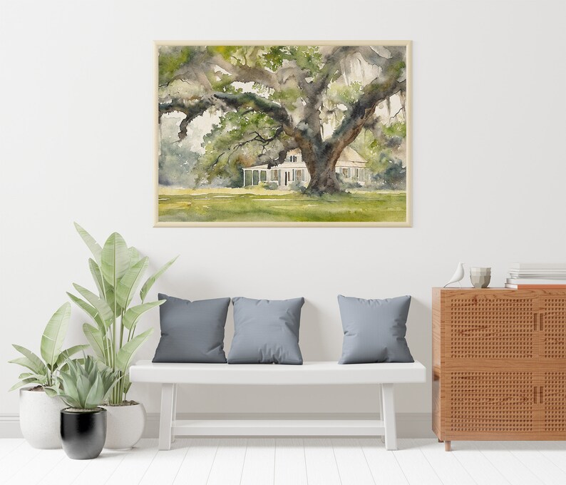May include: A watercolor painting of a white house with a large oak tree in the front yard. The house has a porch and a roof with a slight pitch. The tree has a thick trunk and branches that spread out over the house. The painting is framed in a light brown frame.
