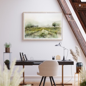Op de afbeelding: Een aquarel schilderij van een landelijk landschap met een zandweg die door een veld met groene bomen en struiken loopt. Het schilderij is ingelijst in een licht houten lijst en hangt aan een witte muur boven een zwart bureau met een stoel.