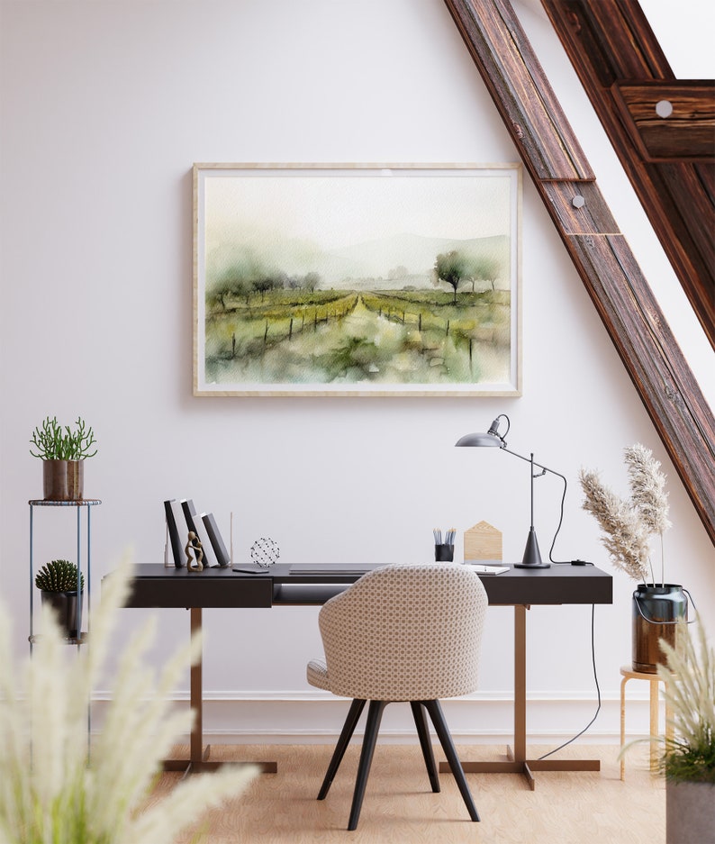 Op de afbeelding: Een aquarel schilderij van een landelijk landschap met een zandweg die door een veld met groene bomen en struiken loopt. Het schilderij is ingelijst in een licht houten lijst en hangt aan een witte muur boven een zwart bureau met een stoel.