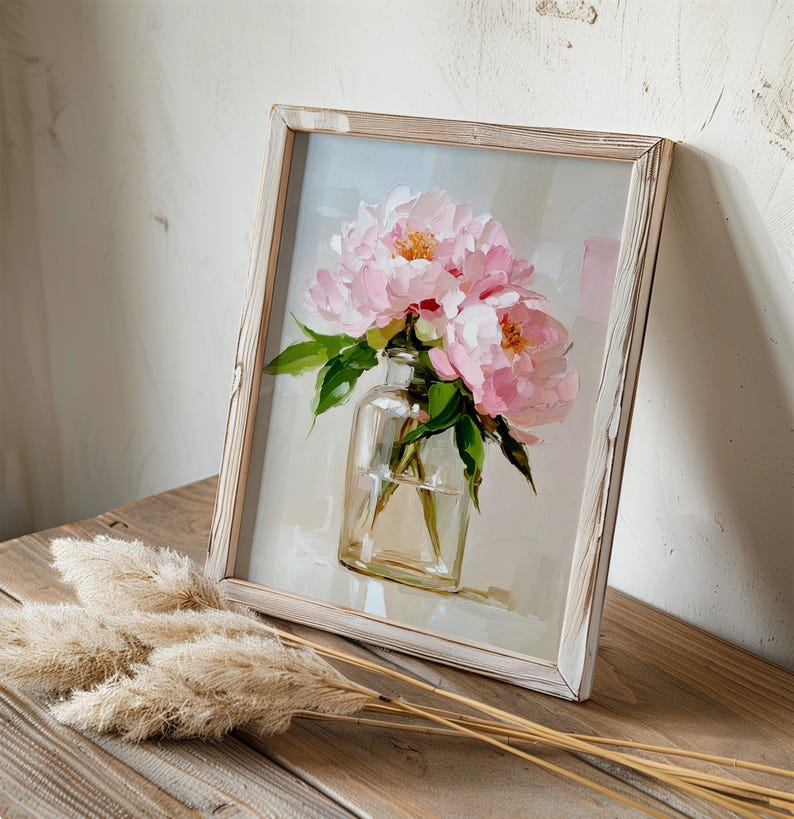 May include: A framed painting of pink peonies in a clear glass vase. The artwork has a light background and is set in a distressed white wooden frame. Green leaves and beige pampas grass are in the foreground.