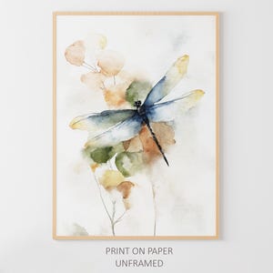 May include: Watercolor print of a dragonfly with blue and yellow wings, perched on a stem with green and brown leaves. The artwork is in a wooden frame. Text at the bottom reads "PRINT ON PAPER UNFRAMED."