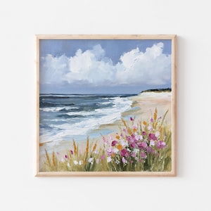 May include: A square oil painting in a light wood frame depicting a coastal scene with a sandy beach, dark blue ocean waves, and a cloudy sky. In the foreground, there are clusters of pink, orange, and yellow wildflowers amidst tall green grass.
