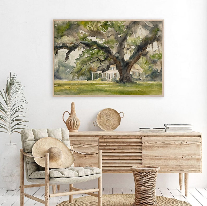 May include: Watercolor painting of a white house with a large oak tree in the front yard. The house has a porch and a green roof. The tree has large branches and green leaves. The painting is framed in a light wood frame.