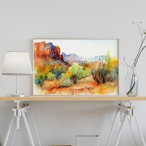 Puede incluir: Pintura acuarela de un paisaje des&eacute;rtico con formaciones rocosas rojas, arbustos verdes y un cielo azul. La pintura est&aacute; enmarcada y colgada en una pared blanca.