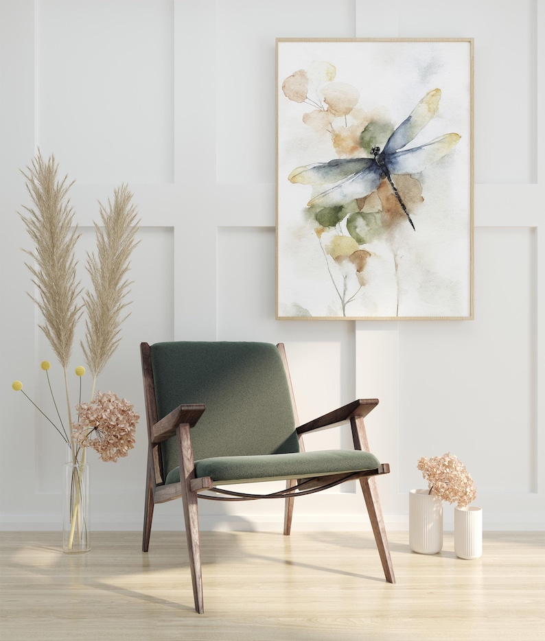 May include: An interior design scene featuring a framed watercolor painting of a dragonfly with a green and blue color scheme. A mid-century modern style chair with a green cushion and wooden frame sits below the artwork. Dried flowers in vases complete the decor.