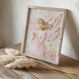 May include: A framed painting of an angel with pink wings and a white dress. The angel is painted in a textured style, giving the painting a three-dimensional look.