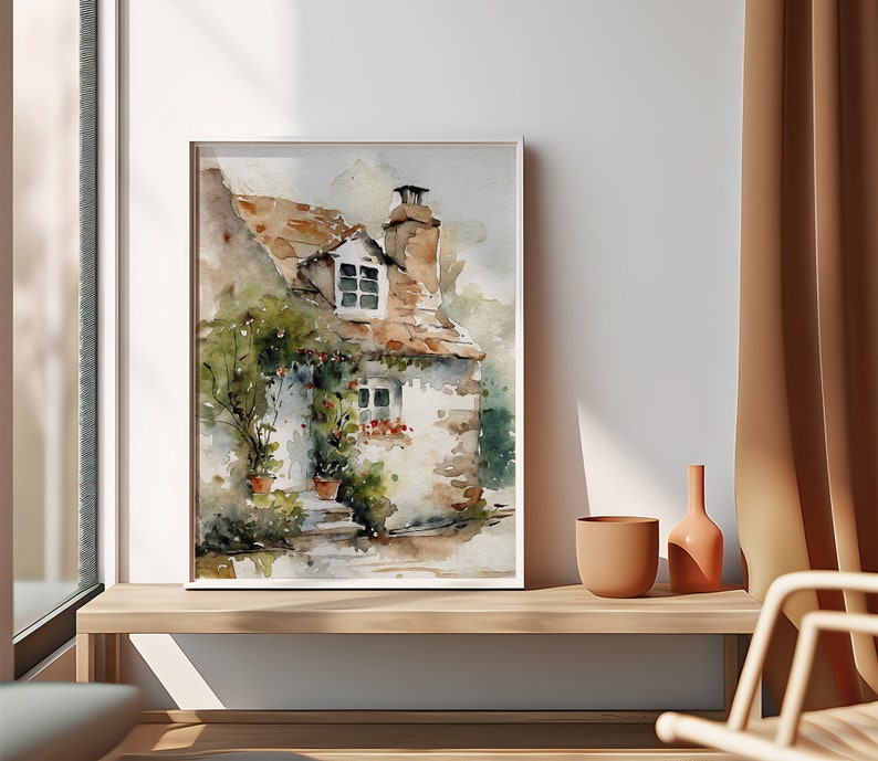 May include: Watercolor painting of a small cottage with a brown roof, white walls, and a window. The cottage is surrounded by green plants and flowers. The painting is framed in a white frame.