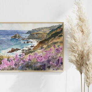 May include: Watercolor painting of a coastal landscape with a rocky shoreline, blue ocean, and a hillside covered in purple wildflowers.