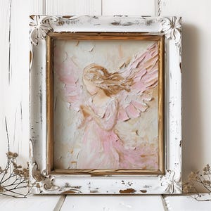 May include: A framed painting of a pink angel with wings, painted in a textured style. The frame is white with gold accents and has a distressed look.