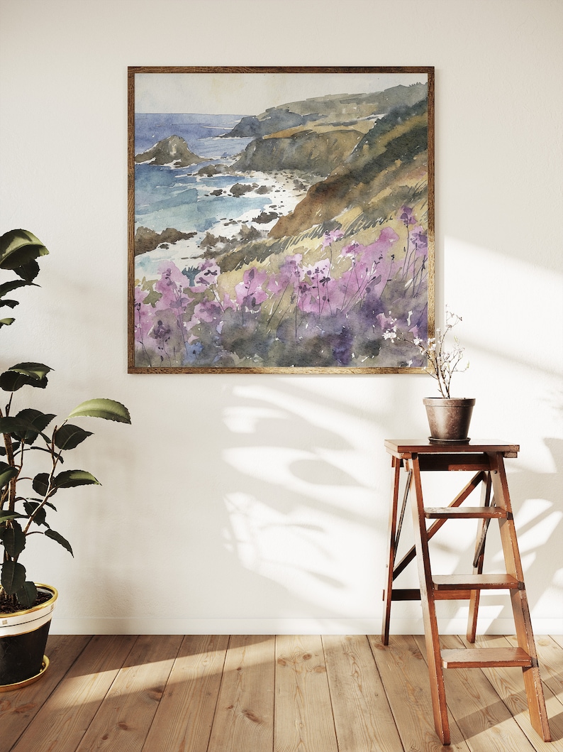 May include: A watercolor painting of a coastal landscape with a rocky shoreline, blue ocean, and purple wildflowers in the foreground. The painting is framed in a wooden frame.