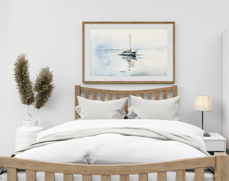 K&ouml;nnte beinhalten: Ein wei&szlig;es Bett mit einem Holz-Kopfteil und einem wei&szlig;en Bettbezug. &Uuml;ber dem Bett h&auml;ngt ein gerahmtes Aquarellbild eines Segelboots. Links neben dem Bett steht eine Vase mit getrocknetem Pampasgras und rechts eine Lampe.
