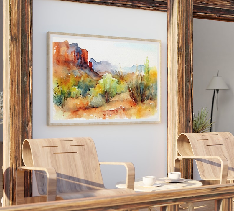 Puede incluir: Una pintura de acuarela de un paisaje des&eacute;rtico con formaciones rocosas rojas, arbustos verdes y un cielo azul. La pintura est&aacute; enmarcada en un marco de madera clara y est&aacute; colgada en una pared blanca.