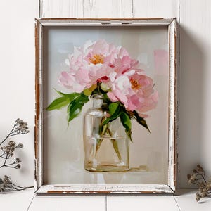 May include: A framed painting of pink peonies in a clear glass vase. The flowers have soft pink petals and yellow centers, with green leaves. The vase sits on a light background, and the frame is white with a distressed finish.
