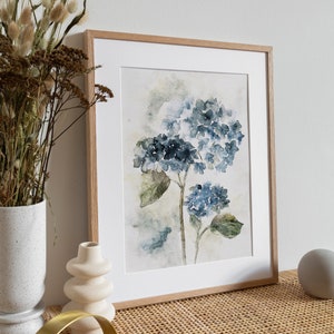 May include: A framed watercolor painting of blue hydrangeas with green leaves on a white background. The frame is made of light wood.