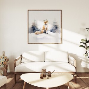 May include: A watercolor painting of a red fox sitting in a snowy forest. The painting is framed in a light wood frame and is hanging on a white wall in a living room setting.