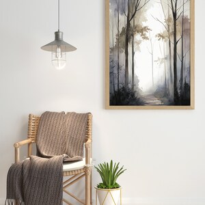 May include: A brown wicker chair with a brown throw blanket draped over it. A white planter with a green succulent plant sits on a gold metal stand. A framed watercolor painting of a forest path hangs on the wall above the chair.