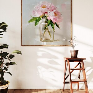 May include: A framed painting of pink peonies in a clear glass vase. The artwork is set against a light background and framed in a brown wooden frame. A potted plant and a wooden step stool are in the foreground.