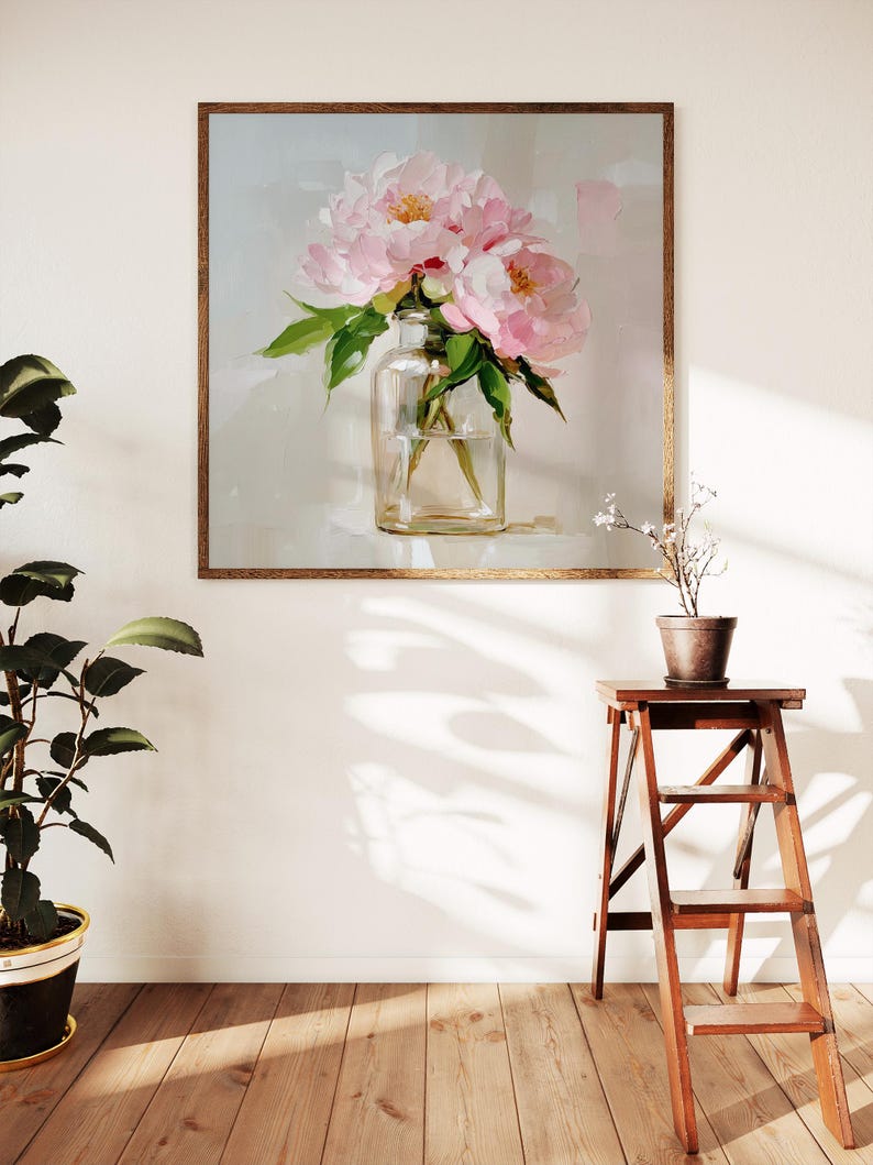 May include: A framed painting of pink peonies in a clear glass vase. The artwork is set against a light background and framed in a brown wooden frame. A potted plant and a wooden step stool are in the foreground.