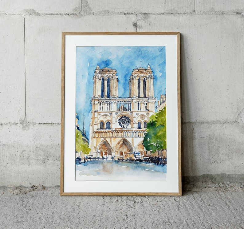 Op de afbeelding: Een aquarel van de Notre Dame kathedraal in Parijs, Frankrijk. De schildering toont de voorgevel van de kathedraal, met zijn twee torens en roosvenster. De schildering is ingelijst in een licht houten lijst.