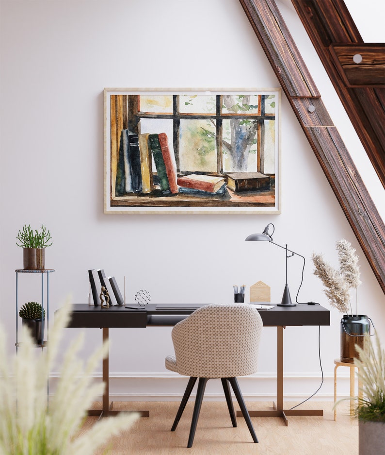 Puede incluir: Una pintura de acuarela de una ventana con vista a los &aacute;rboles y una pila de libros en un alf&eacute;izar de la ventana. La pintura est&aacute; enmarcada en un marco de madera clara y cuelga de una pared blanca sobre un escritorio con una silla.