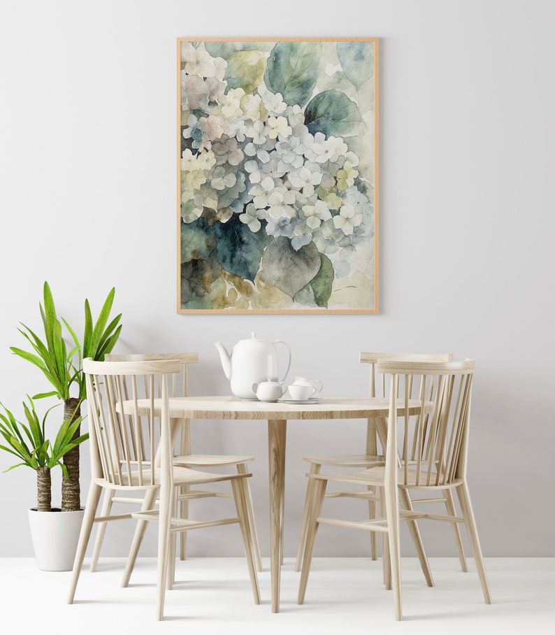 May include: A framed watercolor print of hydrangeas in shades of white, blue, and green. The artwork is displayed above a round wooden table set with a teapot, cups, and chairs. A potted plant is on the left.
