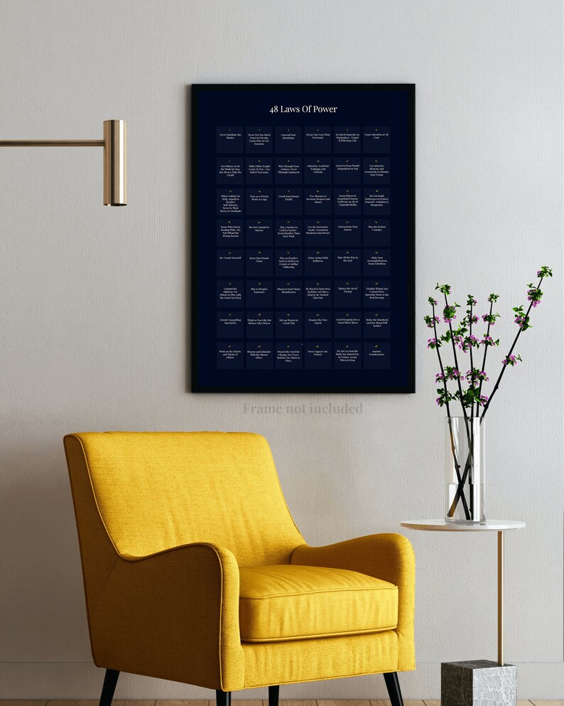 May include: A framed print titled "48 Laws Of Power" hangs on a wall above a yellow armchair. The print has a dark blue background with white text. A small side table with a marble top and a vase of flowers are next to the chair.