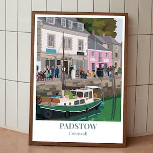 May include: A framed art print featuring a harbor scene in Padstow, Cornwall. The print showcases a green and white boat in the water, with buildings in the background. The print includes the text "PADSTOW Cornwall".