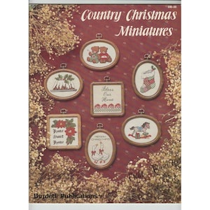 May include: A collection of eight cross-stitch patterns for country Christmas miniatures. The patterns include a stocking, a gingerbread house, a rocking horse, a pair of geese, two bears, and a sign that says "Bless Our Home".