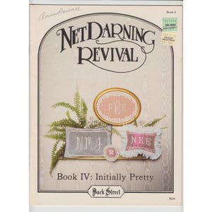 May include: Book cover for Net Darning Revival, Book IV: Initially Pretty. The cover features a pink and white floral design with the title "Net Darning Revival" in a bold font. The book is by Anna Dowell and published by Back Street.
