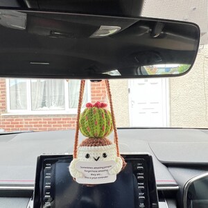May include: A handmade crocheted cactus car air freshener. The cactus is green with brown spots and a red flower. A white tag reads "Sometimes amazing people forget how amazing they are... This is your reminder."