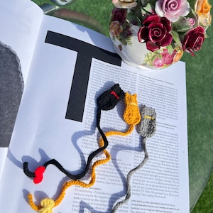 May include: A close-up of a magazine page with text about acting and producing.  There are three crocheted cat bookmarks in black, yellow, and gray.