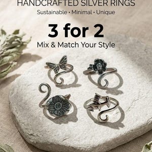 Könnte beinhalten: Handgefertigte Silberringe mit einzigartigen Designs, darunter ein Schmetterling, eine Rose, eine Blume und ein Drache. Die Ringe werden auf einem hellgrauen Stein präsentiert. Der Text "3 für 2" und "Mix & Match Your Style" ist ebenfalls sichtbar.