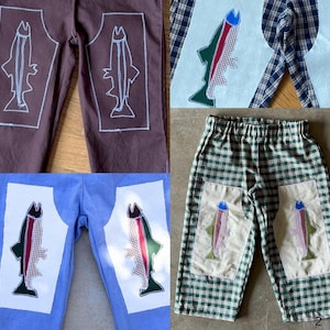May include: A collection of four pairs of pants featuring fish-shaped patches on the legs. The pants include brown, light blue, and green plaid fabrics, with some patches showing white outlines and others displaying colorful checkered fish patterns.